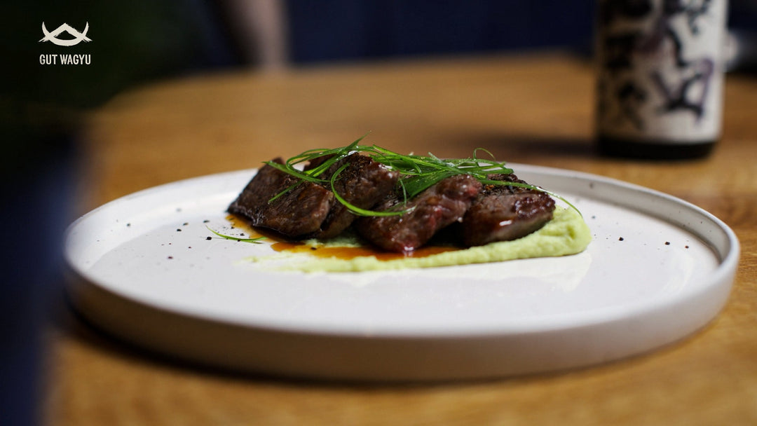 Wagyu Japanese Cut auf Wasabi-Kartoffelpüree garniert mit frischem Frühlingslauch auf weißem Teller.