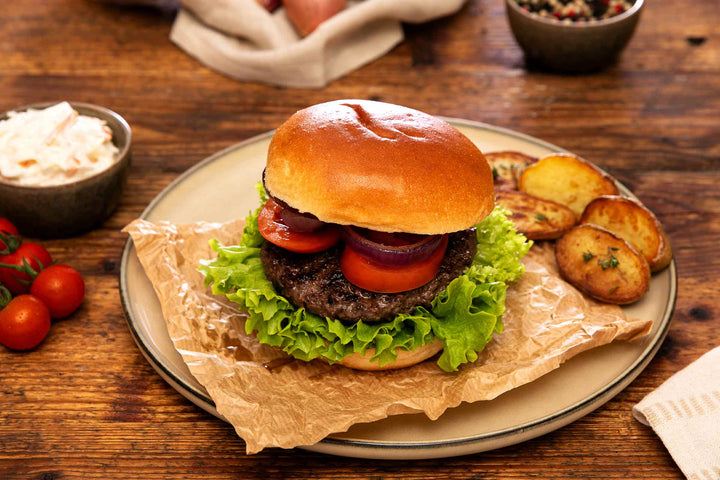 Frisch zubereiteter Wagyu Burger aus deutschem Wagyu-Rindfleisch von Gut Wagyu mit Salat, Tomaten, roten Zwiebeln und gebratenen Kartoffeln.