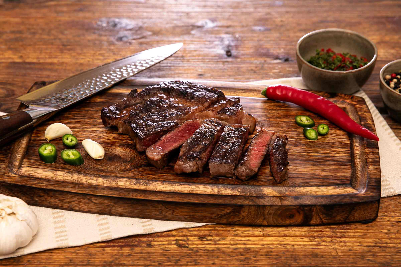 Gegrilltes deutsches Wagyu Entrecôte, in Scheiben geschnitten und auf einem Holzbrett mit Knoblauch und Chili serviert.